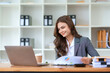 © amnaj - Smiling and attractive asian businesswoman enjoying working using laptop computer at office.