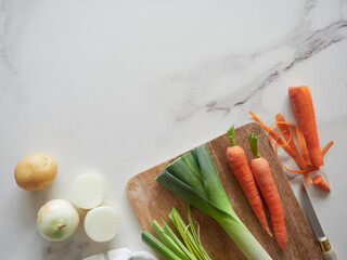 Fresh vegetables for a healthy diet. Carrot, leek, onion and potato on the marble kitchen countertop on wooden board ready to use as cooking ingredients.