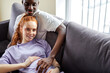 © Roman - Lovely man stroking wife's pregnant belly, lying on sofa at home, relaxing. millennial black man and caucasian woman on comfortable couch, dream of bright happy future together in living room