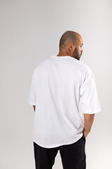 Wall Mural - Back view of a bald african american guy with a beard in a white blank t-shirt. Mock-up.