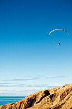 On A Bright Blue Sky A Hang Glider Flies Above The Cliffs In Torrey Pines In La Jolla, California.