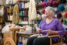 Senior Woman Laughs While Handspinning Wool Into Yarn At A Fiber Arts Studio