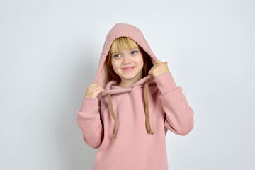 Studio portrait of a cute funny blonde girl in sportswear with a hoodie and trousers on a white background. Fashion. Childhood sportswear advertising. Funny teenage girl in a hoodie
