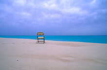A Folding Chair Sits On A Deserted Beach Overlooking A Lagoon.