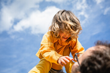 low angle view on smiling child in yellow clothes watching father