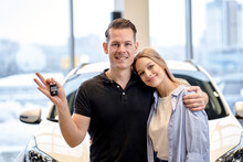 Happy Caucasian Heterosexual Couple Family Husband And Wife Hugging Embracing After Buying New Car Auto At Automobile Dealer Shop Store. Beautiful Blonde Lady And Handsome Guy Holding Key