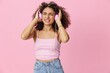 © SHOTPRIME STUDIO - Happy woman wearing headphones with curly hair listening to music and singing along with her eyes closed in a pink T-shirt and jeans on a pink background, copy space