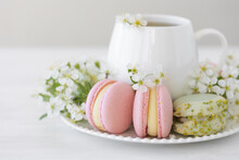 Traditional Delicious French Dessert - Sweet Homemade Macarons On A Vintage Plate. Colourful Tasty Macaroons Served On A White China With Herbal Tea. Decorated With Fragile Cherry Tree Flowers.