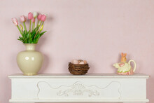 Easter Home Decor - Pink Tulips In Porcelain Vase, Rabbit Shaped Jug And Bird Nest With Eggs On Vintage Rustic White Wooden Fireplace With Pink Painted Wall Background