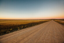Empty Dirt Road Amidst Grassy Field Against Clear Sky During Sunset