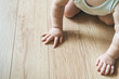 © uladzimirzuyeu - Baby sits on a wooden laminate floor. Bare hands a baby in the living room floor