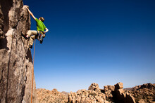 A Male Climber In A Green Shirt Climbs Sail Away (5.8) In The Real Hidden Valley Of Joshua Tree National Park, California.