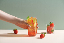 Female Hand Holding Cocktail With Fruits In Glass Cup On Table