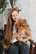 © Alina Hvostikova/Stocksy - Woman with Spitz dog sitting in armchair