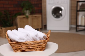 Wall Mural - Wicker basket with folded towels on white table in laundry room. Space for text