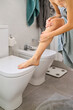 © Guille Faingold/Stocksy - Woman puts cream on leg in bathroom.