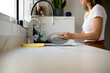 © Guille Faingold/Stocksy - Woman washing plate in kitchen.
