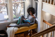 © Raymond Forbes LLC/Stocksy - black Girl relaxing at home reading book in cozy window nook