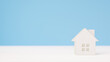 © nanako - 水色の背景に木の小さいおもちゃの家。住宅、不動産、戸建て、新生活のイメージ。（横長）