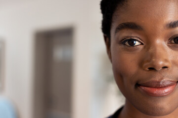 Wall Mural - Half face portrait of smiling african american female doctor in hospital corridor with copy space