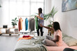 © Studio Marmellata/Stocksy - Black lady sitting on bed near friend hanging clothes