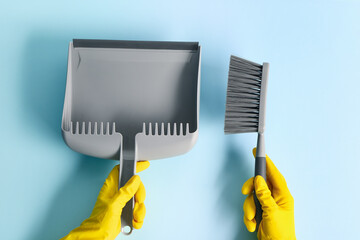 Female hands in rubber gloves with dustpan and brush on color background