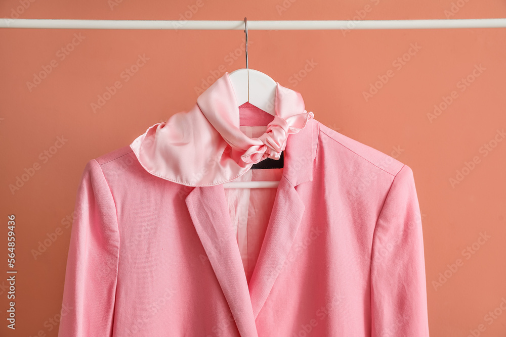 Rack with stylish jacket and scarf near pink wall, closeup