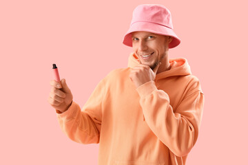 Wall Mural - Thoughtful young man in bucket hat with disposable electronic cigarette on pink background