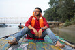 © Dream Lover/Stocksy - Indian young man sitting on boat wearing life jacket