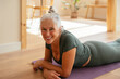 © BONNINSTUDIO/Stocksy - Cheerful senior woman doing fitness on floor