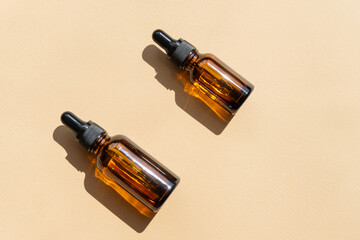 Wall Mural - Top view of amber glass vials with cosmetic serum. Containers without labeling for cosmetics with dropper lids on beige background with hard shadow. Flatley, copyspace