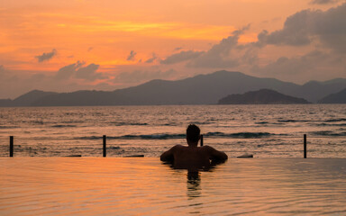 young men at a swimming pool at a luxury hotel, a Luxury swimming pool in a tropical resort, relaxing holidays. A young man during sunset by swim pool, men watching a sunset in an infinity pool