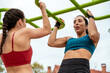 © David Prado/Stocksy - Athletic ladies doing pull ups on bars in park