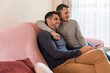 © Luis Velasco/Stocksy - Cute Gay Couple Watching TV On The Couch.