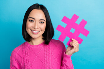 Poster - Portrait of pretty cheerful girl beaming smile hand hold paper hashtag card isolated on blue color background