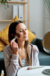 © nomad studio/Stocksy - Woman applying make-up in living room.
