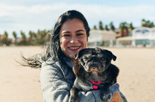 Smiling Woman Holding Her Pug At The Beach