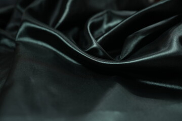 Black satin fabric background with wavy soft folds for selling product. Black Texture - Dark Wavy Glossy Silk Drapery. Black silk satin. Shiny smooth fabric. Elegant background for design.