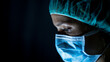© Cavan Images - Portrait of young female surgeon, wearing mask and a surgical mask, in front of black background