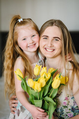 Wall Mural - Mother's day concept. Girl congratulates mother and gives a bouquet of yellow flowers tulips at home. Mom and daughter smiling and hugging. Holiday greeting card for International Women's Day. Closeup