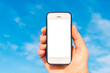 © ARVD73 - A Mans hand holding smartphone on blue sky nature background,sunny day. Mockup white screen smart phone.Copy space.