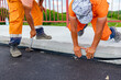 Workers apply black bitumen membrane strips for waterproofing roads and bridges to the curb of the sidewalk