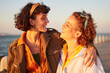 © Alexis S/peopleimages.com - Lesbian, lgbtq and couple of friends at the beach with love, hug and excited for summer holiday and date. Sunset, sea and smile of women or gay people with pride, freedom and gen z solidarity in sun