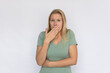 © Mangostar - Shocked young woman covering mouth. Portrait of happy Caucasian female model with fair hair in green T-shirt looking at camera with wide eyes, receiving news. Shock, gossip concept