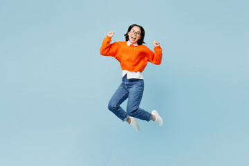 Wall Mural - Full body fun young woman of Asian ethnicity wear orange sweater glasses jump high do winner gesture clench fist isolated on plain pastel light blue cyan background studio. People lifestyle concept.