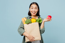 Young Surprised Woman Wear Casual Clothes Hold Apple Brown Paper Bag With Food Products After Shopping Isolated On Plain Blue Cyan Background Studio Portrait. Delivery Service From Shop Or Restaurant.