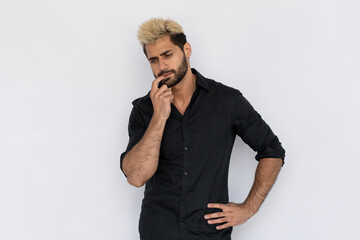 Portrait of thoughtful young man biting finger over white background. Caucasian guy with stubble and highlighted hair wearing black T-shirt thinking over problem. Thinking and planning concept