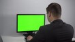 © Vital9c - A young businessman is sitting in front of a computer with a green screen. A man in a suit works for a PC. Screen with chroma key.