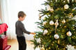 © Cavan Images - Young boy stands placing ornament on Christmas tree during holiday