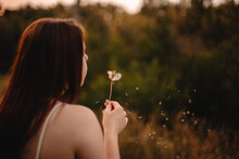 Carefree Teenage Girl Blowing Dandelion At Sunset In Summer
